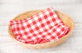 Wicker basket with a red checked cotton napkin inside on a white wooden table Royalty Free Stock Photo