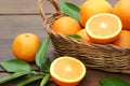 Wicker basket, ripe juicy oranges and green leaves on wooden table, closeup