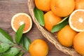 Wicker basket, ripe juicy oranges and green leaves on wooden table, flat lay Royalty Free Stock Photo