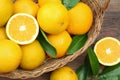 Wicker basket, ripe juicy oranges and green leaves on wooden table, flat lay Royalty Free Stock Photo