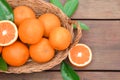 Wicker basket with ripe juicy oranges and green leaves on wooden table, flat lay. Space for text Royalty Free Stock Photo