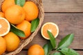 Wicker basket, ripe juicy oranges and green leaves on wooden table, flat lay Royalty Free Stock Photo