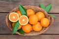 Wicker basket with ripe juicy oranges and green leaves on wooden table, top view Royalty Free Stock Photo