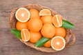 Wicker basket with ripe juicy oranges and green leaves on wooden table, top view Royalty Free Stock Photo