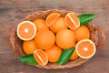 Wicker basket with ripe juicy oranges and green leaves on wooden table, top view Royalty Free Stock Photo