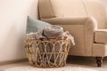 Wicker basket with rolled blankets and pillow near sofa. Idea for interior design