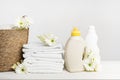 Wicker basket with white linen, washing gel and fabric softener on a white table with gerbera flowers. Mockup spring laundry day