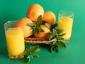 Wicker bowl with oranges decorated with mint, next to a glass with orange juice on a green background