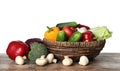 Wicker bowl with variety of fresh delicious vegetables and fruits on table against white