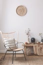 Wicker chair with striped pillow on it next to wooden table full of accessories such as vase, flowers and candles Royalty Free Stock Photo