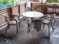 Wicker chairs stand around a white round table on a wooden floor wet after rain in an outdoor cafe Royalty Free Stock Photo