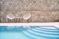 Wicker chairs with a table stand near the stone wall by the pool