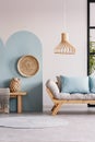 Wicker chandelier above wooden Scandinavian sofa with futon in bright living room interior Royalty Free Stock Photo