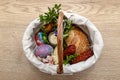 A wicker Easter basket filled with food standing on a table, decorated with boxwood and catkins.