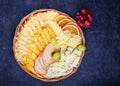 Wicker flat basket with a delicious variety of cheese, dried orange and apple slices on a dark background