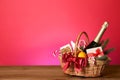 Wicker gift basket with wine on wooden table against pink background, space for text Royalty Free Stock Photo