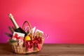 Wicker gift basket with wine on wooden table against pink background, space for text Royalty Free Stock Photo