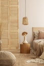 Wicker lamp above wooden nightstand with flowers in a vase i stylish bedroom interior with beige design