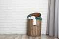Wicker laundry basket full of dirty clothes near brick wall in room Royalty Free Stock Photo