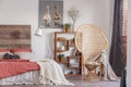 Wicker peacock chair with blanket in fashionable rustic bedroom with bookshelf and king size bed with bedhead Royalty Free Stock Photo