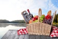 Wicker picnic basket with wine and products on wooden table near lake, space for text Royalty Free Stock Photo