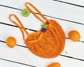 wicker purple bag with oranges lies on a white wood background with a green