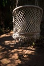 A wicker suspended summer chair hangs in the shade of tropical trees.