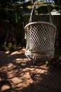 A wicker suspended summer chair hangs in the shade of tropical trees.