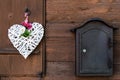 A wicker white heart with peonies and daisies hangs on a wooden shutter and a mailbox next to it