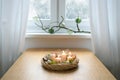Wicker willow advent wreath with white candles, the third one is lit, decoration from Christmas balls, cookies and moss on a table Royalty Free Stock Photo