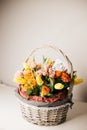 Wicker wooden basket with bouquet of orange and pink roses and yellow tulips and a business card against a white wall and table. Royalty Free Stock Photo