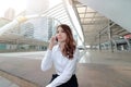 Wide angel shot of attractive young Asian business woman sitting on staircase and talking on phone at city background.