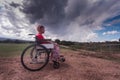 Wide angle disabled girl sitting in a wheelchair in the middle of a green field in the countryside with a sky clouds Royalty Free Stock Photo