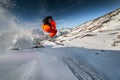 Wide angle male skier in orange suit makes a jump from a snowy ledge in the mountains. Snow powder trailing behind the Royalty Free Stock Photo