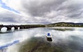 Wide angle photo of a stone bridge crossing the bay of Pontedeume in La Coruna, Spain with a boat in the foreground, mountains wi Royalty Free Stock Photo