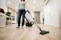 Wide angle photo of woman housewife or maid or service worker hoovering with vacuum cleaner in bright luxury appartment.