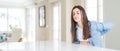 Wide angle picture of beautiful young woman sitting on white table at home Suffering of backache, touching back with hand,