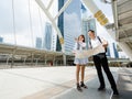 Wide-angle portrait cute smiling young Asian couple tourists standing and holding a paper city map on footbridge together while