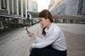 Wide angle shot of attractive young Asian business woman looking mobile smart phone in her hands at outside office with copy space Royalty Free Stock Photo