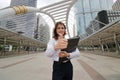 Wide angle shot of cheerful young Asian business woman showing thumb up with document folders on her hand at urban background. Royalty Free Stock Photo