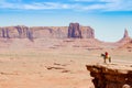 Wide-angle shot of a cool cowboy sitting on a horse on the edge of a cliff in Monument Valley