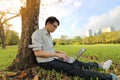 Wide angle shot of happy young man typing on a laptop computer for his work in a beautiful city park. Royalty Free Stock Photo