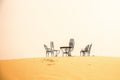 Wide angle shot of several chairs and a table put on the sand in a desert Royalty Free Stock Photo