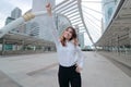 Wide angle shot of successful young Asian business woman raising her hand and smiling at urban building background Royalty Free Stock Photo