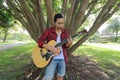 Wide angle shot of young hipster man playing music on acoustic guitar in a beautiful nature background. Royalty Free Stock Photo