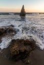 Ocean waves crashing into rocks on beach sand with tall point rock off coast shore Royalty Free Stock Photo