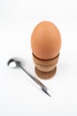 Wide angle vertical shot of hen egg in old wooden egg stand with metal spoon, isolated on white background. Breakfast minimalistic Royalty Free Stock Photo