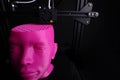 Wide angle view on a 3D printer manufacturing a humanoid head from pink plastic in dark light