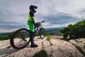 A wide angle of a young mountain bike rider in a helmet and a protective suit on his mountain bike stands on a rock Royalty Free Stock Photo