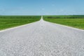 A wide asphalt road between green fields